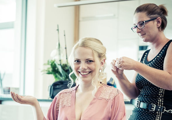 Friseurin stylt Kundin im rosa Spitzenmantel eine Hochsteckfrisur